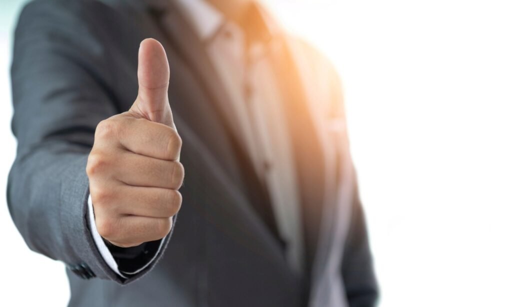 Buste d’un cadre dirigeant en costume cravate, de profil, levant le pouce vers le haut pour symboliser une négociation réussie et un départ positif.