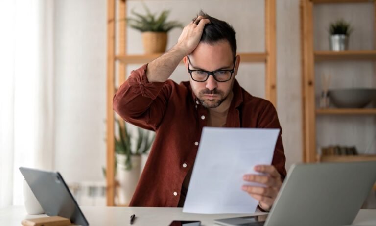 Homme assis à son bureau se grattant la tête en regardant des documents, illustrant la complexité du calcul de l’allocation chômage (ARE)